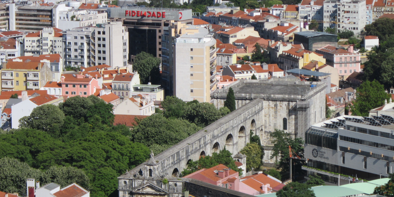 Stone aqueduct running through a hillside city of red-tiled roofs and apartment blocks — The Portugal Move Kit